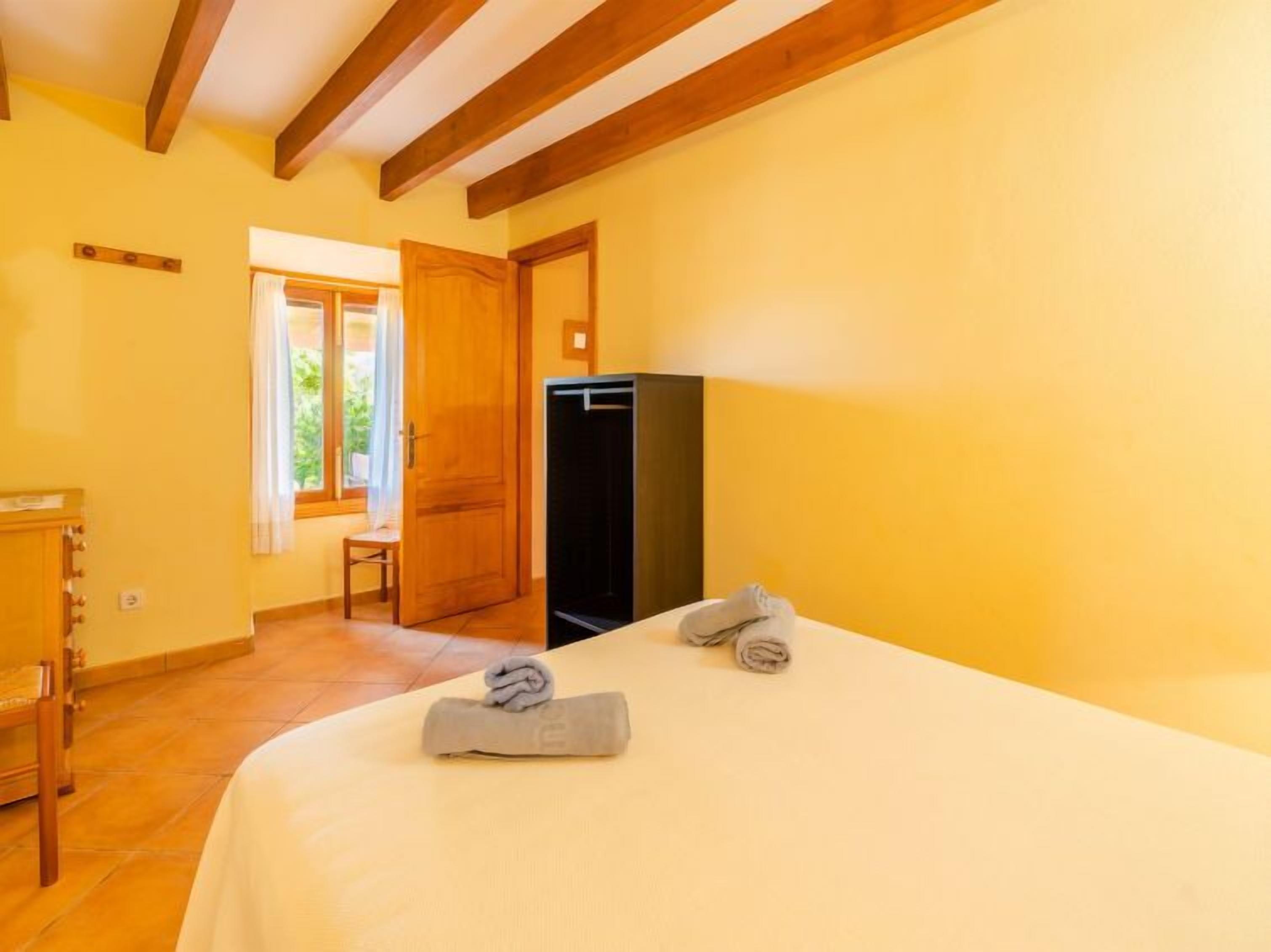 A room with a bed, a wooden wardrobe, a small table, and a door leading to another room.