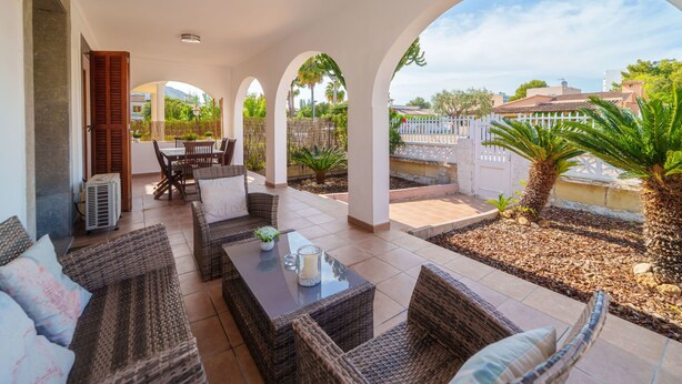 Eine überdachte Terrasse im Freien mit Rattanmöbeln, einem Esstisch und Blick auf die Umgebung.