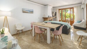 Ein modernes Zimmer mit einem Holzesstisch, rosa Stühlen, einem Bett mit grüner Bettdecke, einem Fernseher und einem Fenster mit Vorhängen.