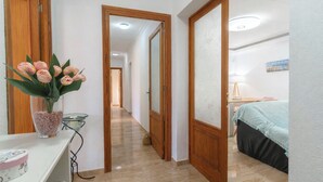 Ein Flur, der in ein Schlafzimmer mit Bett, Nachttisch und Beistelltisch führt.