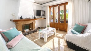 Ein Wohnzimmer mit Kamin, Fernseher und einem großen Fenster mit Vorhängen.
