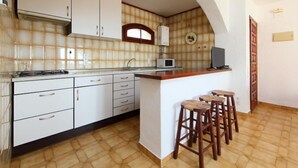 A kitchen with white cabinets, a microwave, and a small bar area with stools. - Peces 3 by Interhome (Peñiscola)