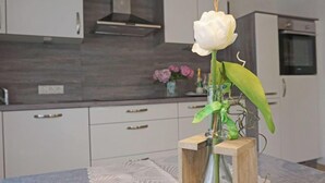 Une cuisine avec des armoires blanches, une hotte de cuisinière en acier inoxydable et une table en bois sur laquelle est posé un vase de fleurs.