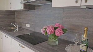 Une cuisine moderne avec un plan de travail foncé, un évier en acier inoxydable, un vase avec des fleurs roses et une bouteille de champagne accompagnée de verres, le tout posé sur un chemin de table.