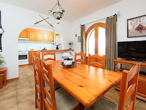 Un comedor con una mesa y sillas de madera, un televisor y una cocina al fondo.
