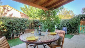 A covered patio with a round table set for four, surrounded by wooden chairs. - Les Marines du Roussillon by Interhome (Saint Cyprien)