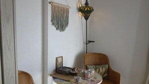 A cozy corner with wicker chairs, a small round table with a floral tablecloth, a hanging macrame wall hanging, and a tall floor lamp. - Les Marines du Roussillon by Interhome (Saint Cyprien)