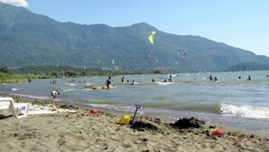 Een strand met mensen die watersporten beoefenen en vliegeren, met bergen op de achtergrond.