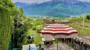 Een terras met tafel, stoelen en parasol met uitzicht op een bergachtig landschap.