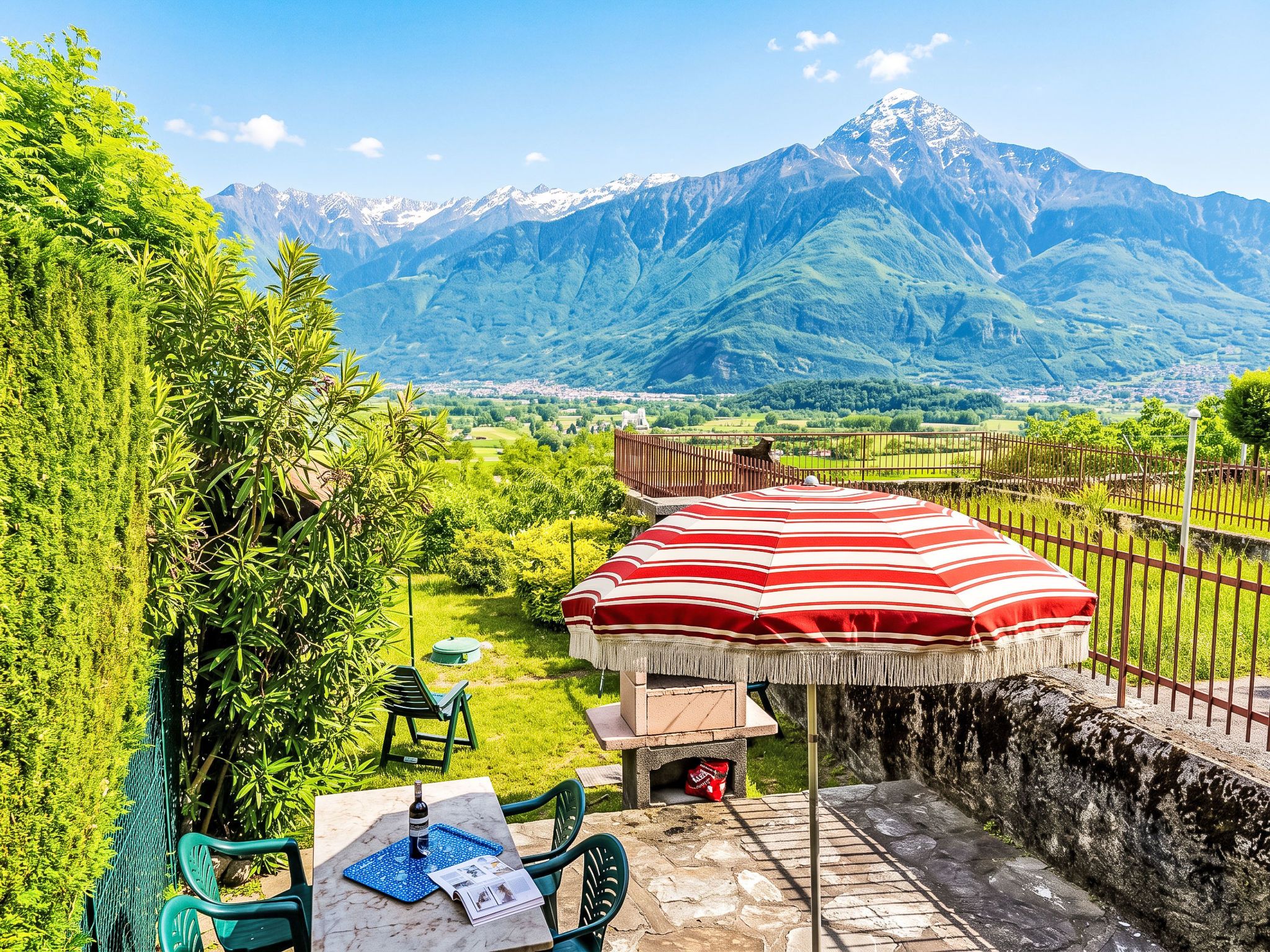 Een terras buiten met een tafel, stoelen en een gestreepte parasol, met uitzicht op een bergachtig landschap.