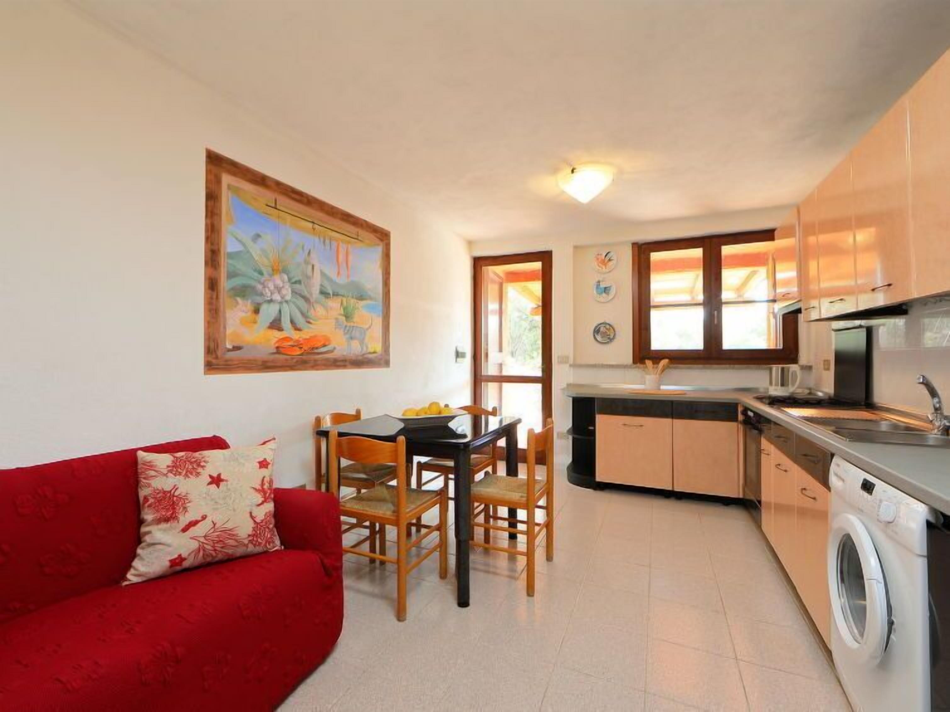 Un espacio habitable compacto con comedor, un sofá rojo, una cocina con lavadora y un cuadro en la pared.