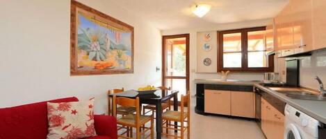 Un espacio habitable compacto con comedor, un sofá rojo, una cocina con lavadora y un cuadro en la pared.