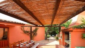 Une terrasse extérieure dotée d’un espace repas couvert, d’un barbecue et d’un sol carrelé.