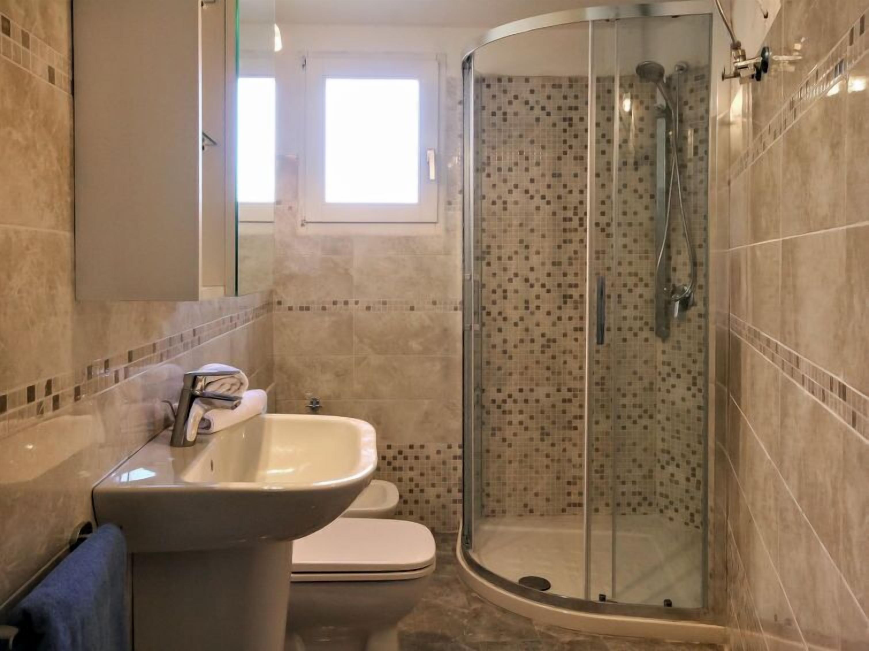 Un bagno con doccia vetro, lavandino e WC.