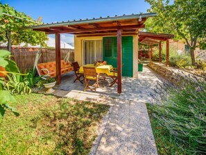 A covered patio with a table and chairs, surrounded by plants and a wooden fence.
