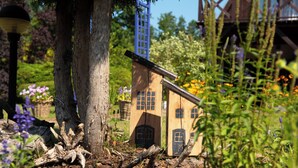 A model house with a pitched roof and a chimney, surrounded by trees and flowering plants.