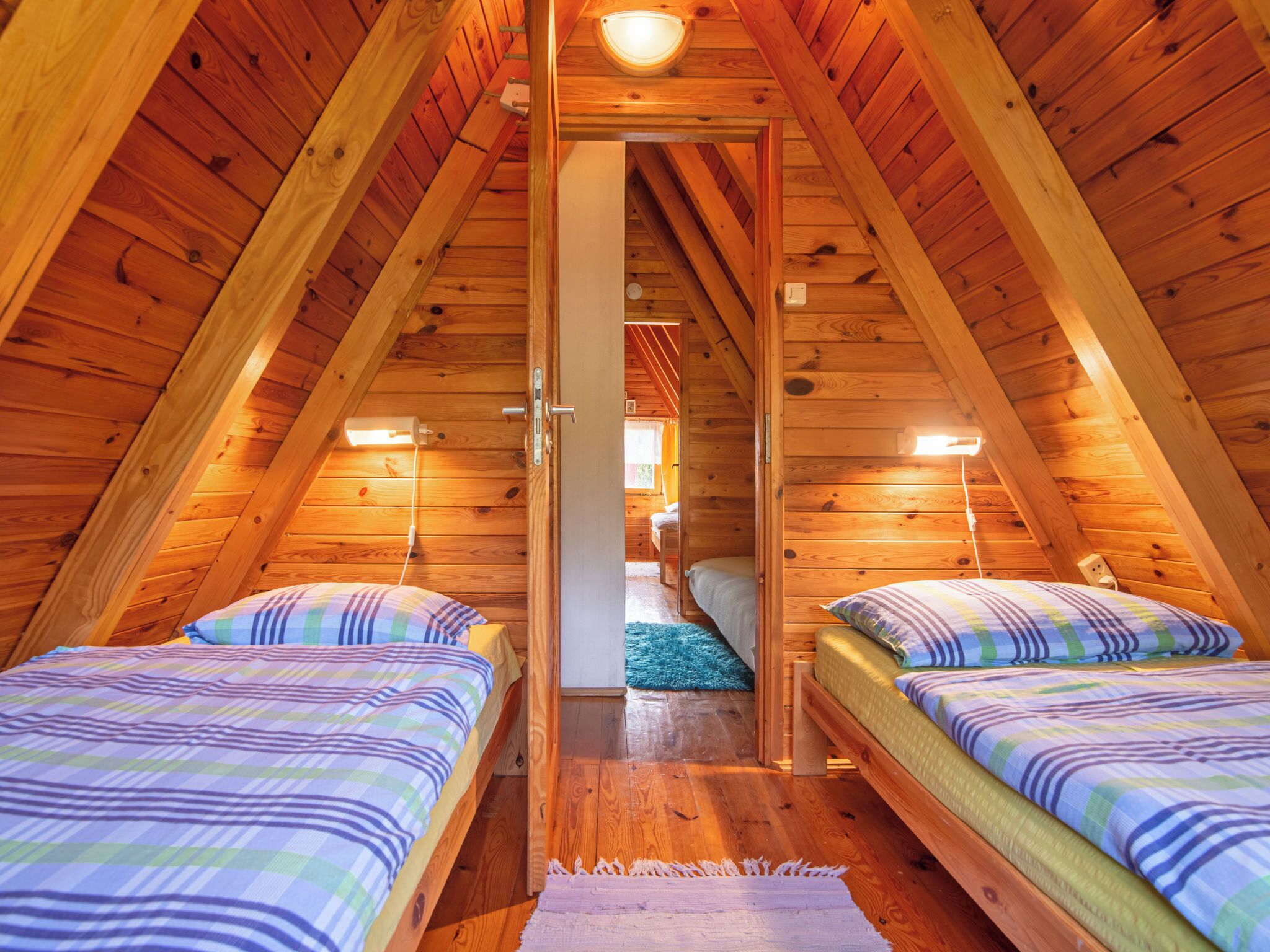 A cozy attic bedroom with two beds, wooden walls, and a sloped ceiling.