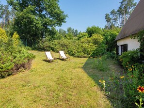 A grassy outdoor area with two lounge chairs, surrounded by trees and a building with a sloped roof.