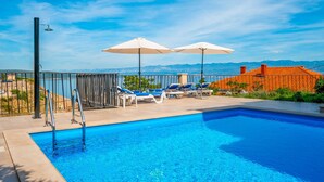 Una piscina con tumbonas y sombrillas, rodeada por una valla y con vistas panorámicas.