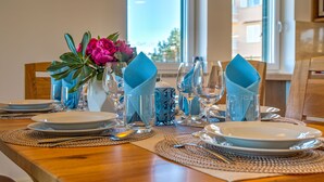 Una mesa de comedor dispuesta con platos, vasos y servilletas azules, con un jarrón de flores y vistas a edificios.