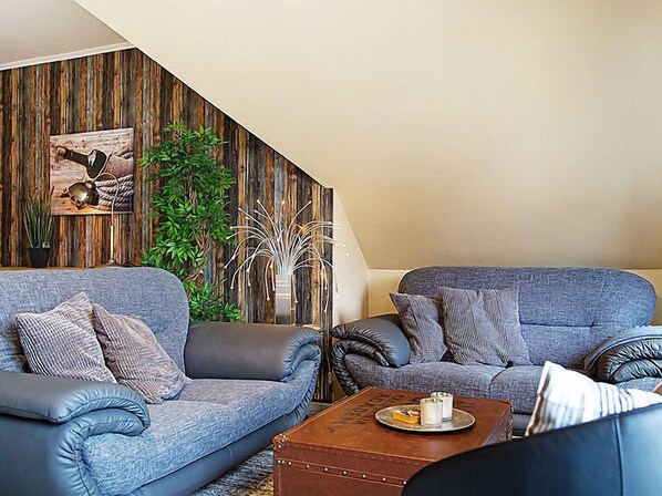 A living room with two grey sofas, a wooden accent wall, a painting, and a potted plant.