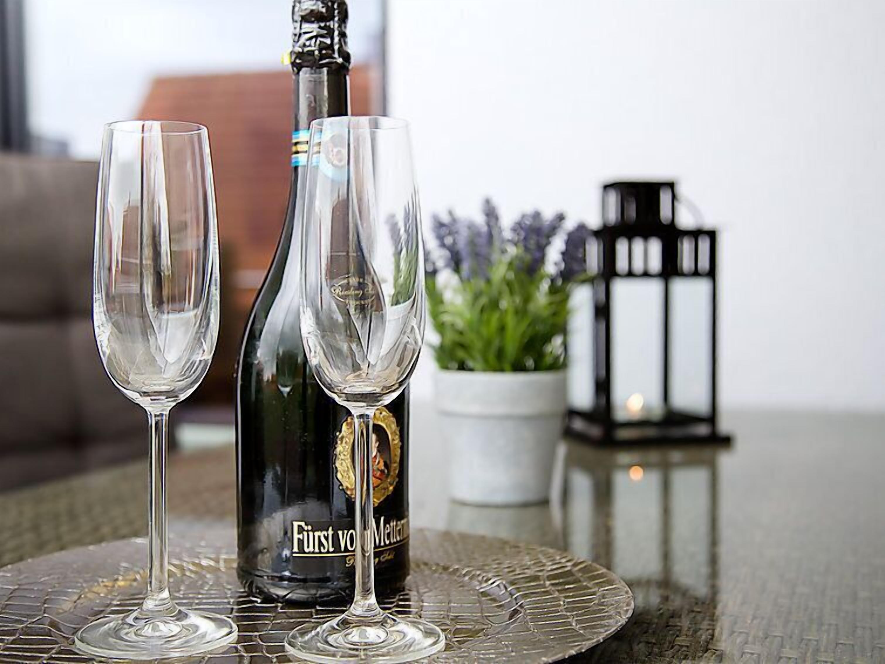 Two empty wine glasses on a glass table with a bottle of Fürst von Mettern wine and a small potted plant in the background.