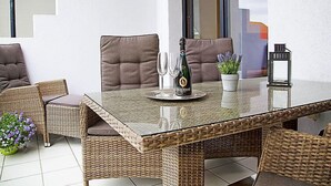 A dining area with wicker furniture, a glass table, and a bottle of champagne. - Witthuus-Langeoog by Interhome (Norddeich)