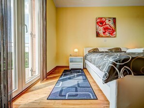 A bedroom with a bed, a nightstand, a lamp, a painting, and a view through the window.