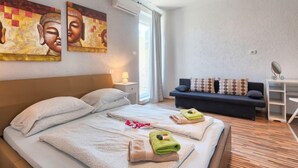 Hotellihuone, jossa on sänky, kaksi taulua seinällä, sohva ja pieni pöytä, jossa on lamppu.