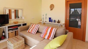 Una sala de estar con un sofá color crema, almohadones a rayas, un televisor, una mesita y un espejo.