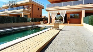 Una casa moderna de dos pisos con piscina, mobiliario exterior y un patio cubierto.
