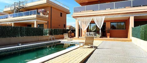 Ein modernes, zweistöckiges Haus mit Swimmingpool, Außenbereich zum Sitzen und einer überdachten Terrasse.