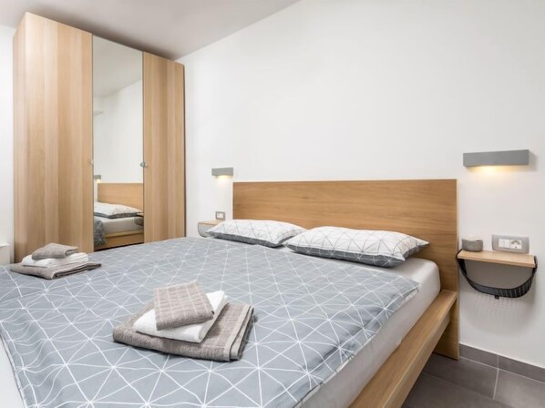 A modern bedroom with a large bed, wooden headboard, and a nightstand with a lamp.