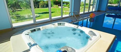 A hot tub with a view of a swimming pool and a garden.