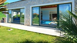 Ein modernes Haus mit großen Glasfenstern, einem Swimmingpool und einem gepflegten Rasen.