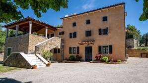 A two-story building with a stone facade, a covered porch, and a gravel driveway. - Kapitani by Interhome (Hum)