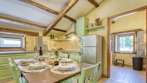 A cozy kitchen with a dining table set for four, wooden beams on the ceiling, and a stone wall. - Kapitani by Interhome (Hum)