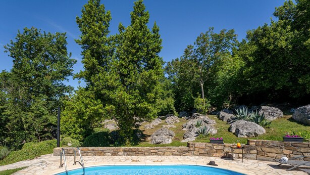 A swimming pool with a stone border, surrounded by trees and rocks. - Kapitani by Interhome (Hum)