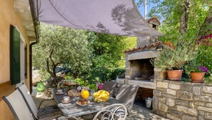 An outdoor patio with a stone oven, a table set with food and drinks, and potted plants. - Kapitani by Interhome (Hum)