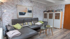 Una sala de estar moderna con un sofá gris, una mesa de centro de vidrio y una pared con diseño de ladrillo.