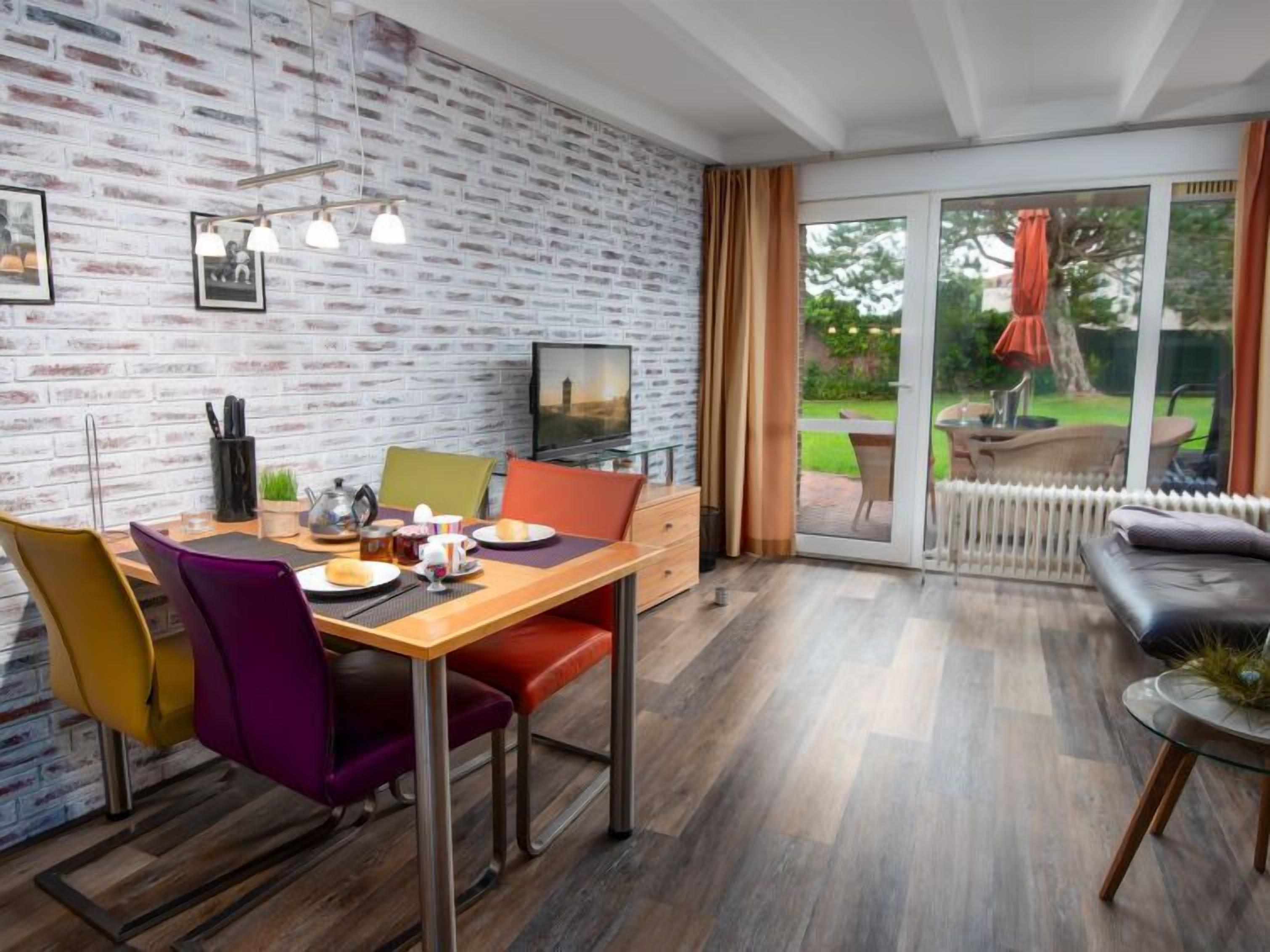 Un comedor moderno con pared de ladrillo, televisión y puerta corrediza de vidrio que da a un patio al aire libre.