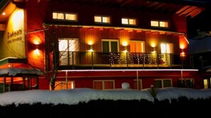 Un immeuble de deux étages avec une façade rouge, de nombreuses fenêtres et un balcon décoré de guirlandes lumineuses.