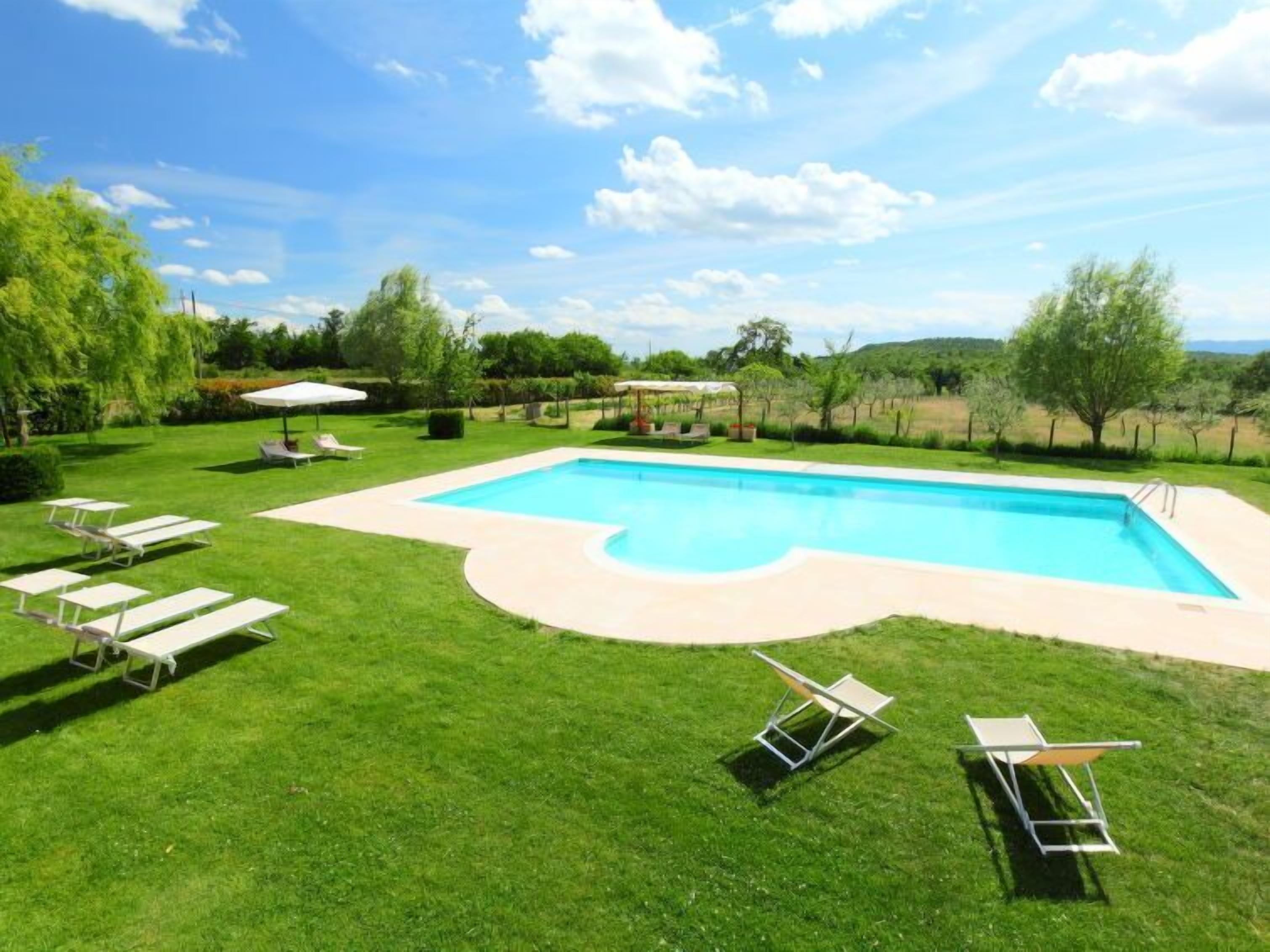 A rectangular swimming pool with a curved edge, surrounded by a well-maintained lawn and several lounge chairs.