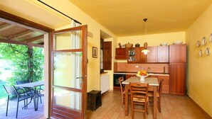 Une cuisine avec des meubles en bois, une table à manger avec des chaises et une vue sur l’extérieur grâce à une porte vitrée.