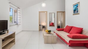 A modern living room with a flat-screen TV, a red sofa, a coffee table with fruits, and a painting on the wall. - Apartment Tea by Interhome (Krk/Šilo)