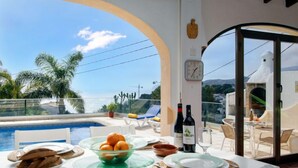 Espaço de refeições com vista para a piscina e palmeiras, um relógio e uma escultura de pássaro branco.