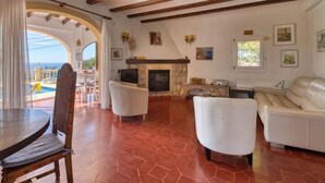 Uma sala de estar ampla com lareira, sofás brancos, televisão e vista para a piscina.