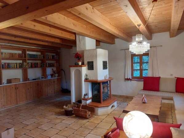 A cozy living room with wooden beams, a fireplace, a bookshelf, and a window with curtains. - Waldhaus by Interhome (Kollnburg)