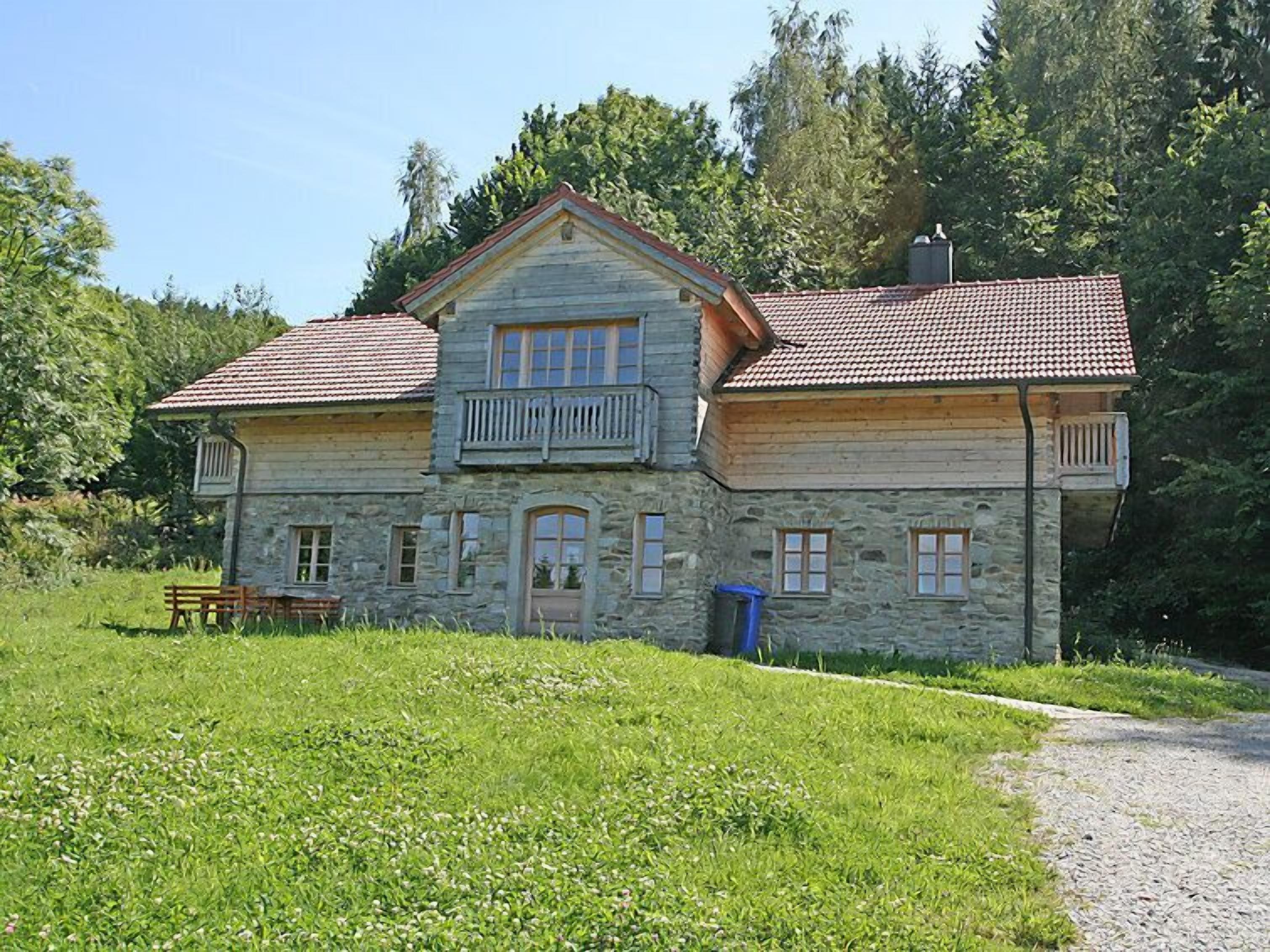 Une maison en pierre avec un toit recouvert de tuiles rouges, un balcon et une pelouse devant.