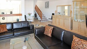 Un salon moderne avec des canapés en cuir, une table basse en verre et un escalier en bois menant à un espace repas.